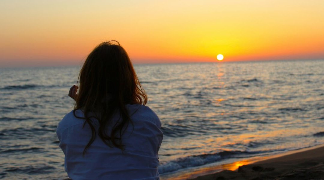 woman facing toward the ocean during sunset